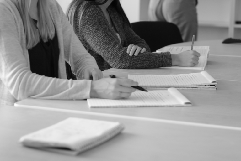 Black and white image of students writing notes during a meeting.